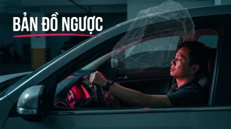 Người đàn ông ngồi ghế lái trong gara tối, mắt nhắm, kiệt sức; một tảng đá bán trong suốt đè trên nóc xe, bảng điều khiển hắt ánh hồng đỏ lên mặt, kèm chữ “BẢN ĐỒ NGƯỢC”.